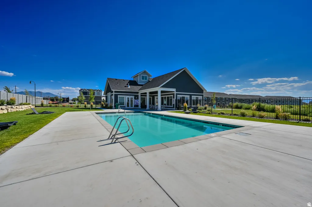 Rectangular swimming pool with metal handrails, surrounded by a concrete pool deck and grassy areas