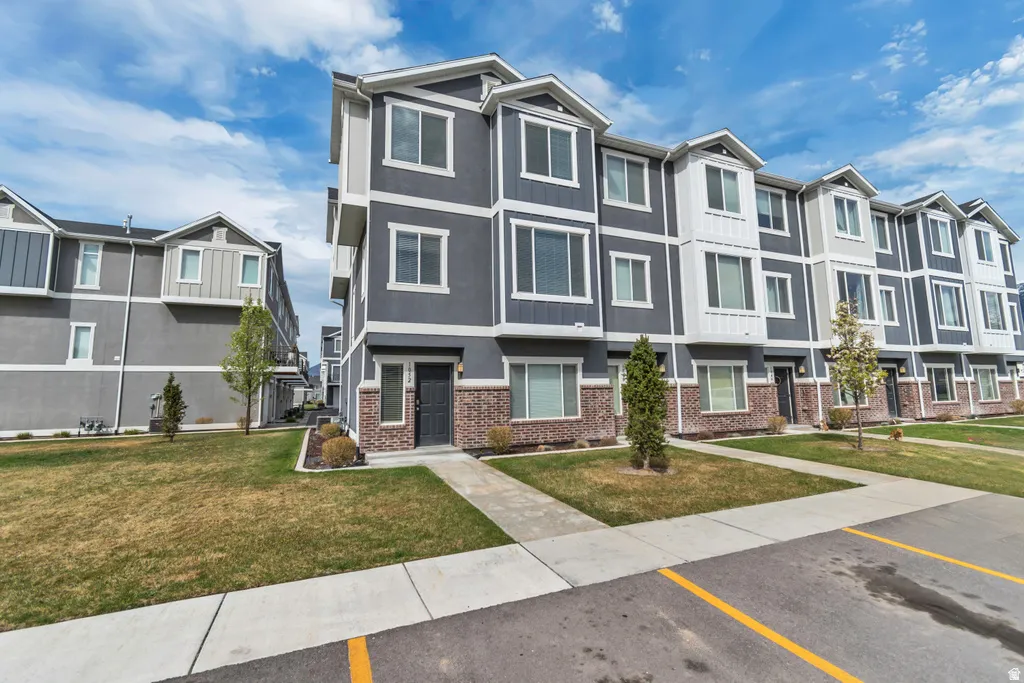 Modern townhome exterior with gray siding, white trim accents, brick detailing, multiple windows, and a paved walkway