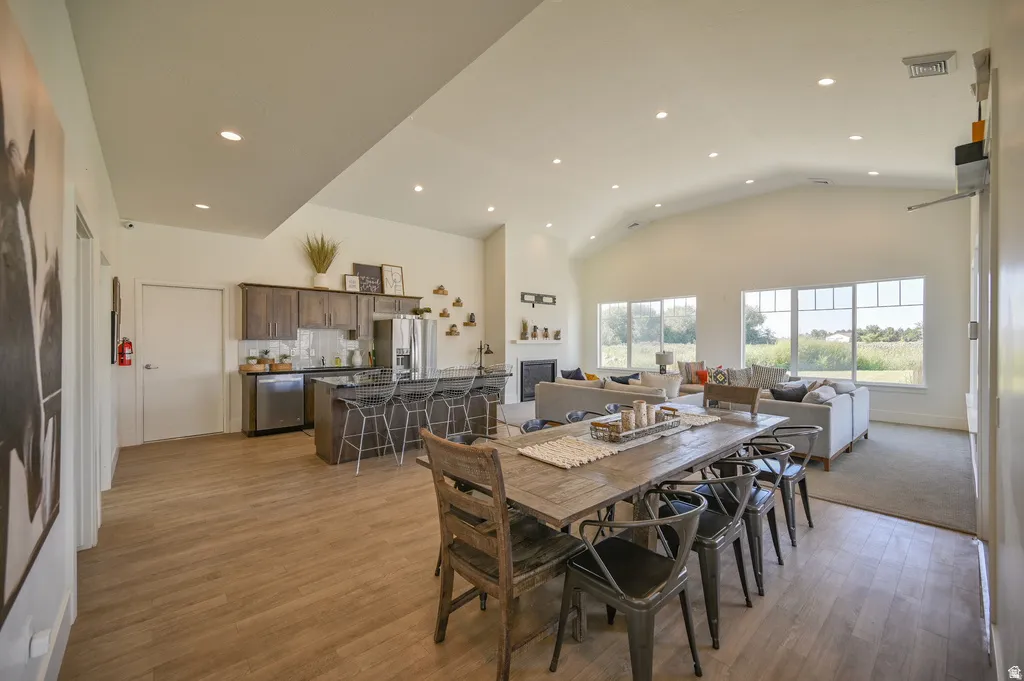Vaulted ceilings with recessed lighting, wood-finish flooring, a kitchen island with dark cabinetry, stainless steel appliances, and a fireplace