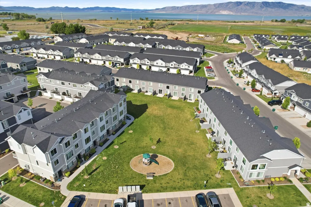 Aerial perspective showcasing multiple two and three-story townhome buildings, a central green space with a playground, and nearby surface parking