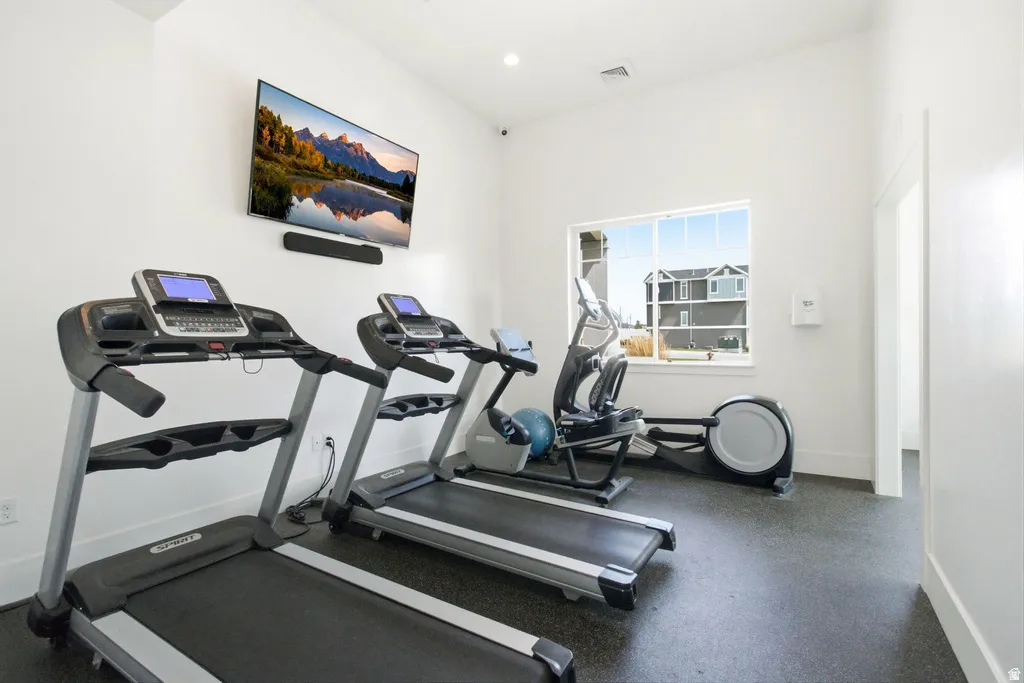 Dedicated fitness space featuring rubberized flooring, a wall-mounted display, and a window with exterior views