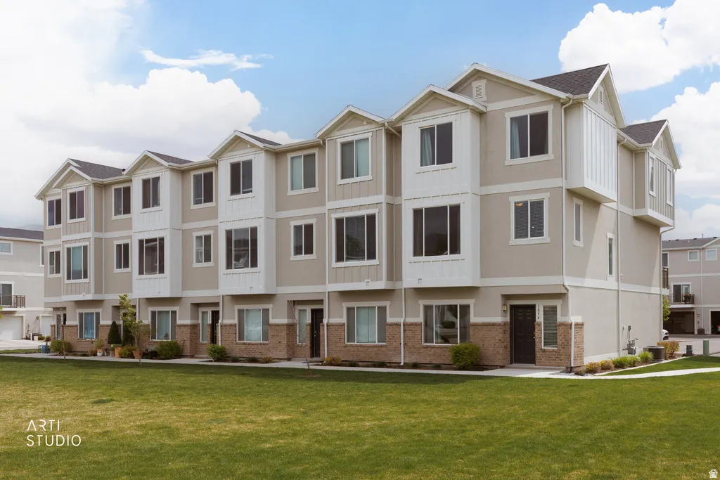Contemporary townhome architecture featuring multiple bay windows, a dark shingle roof, and a combination of light-toned siding with brick accents