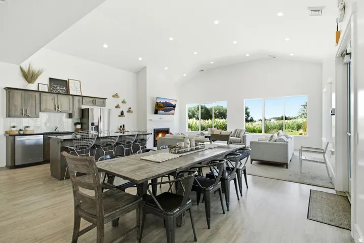 Vaulted ceiling with recessed lighting, integrated kitchen appliances, kitchen island with counter seating, large dining area, and a fireplace with a mantel