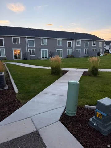 Expansive green space featuring a concrete pathway, mature landscaping, and multi-level residences with individual patios