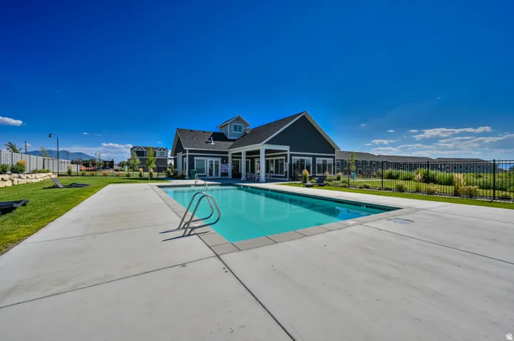 Rectangular swimming pool with metal handrails, surrounded by a concrete pool deck and grassy areas