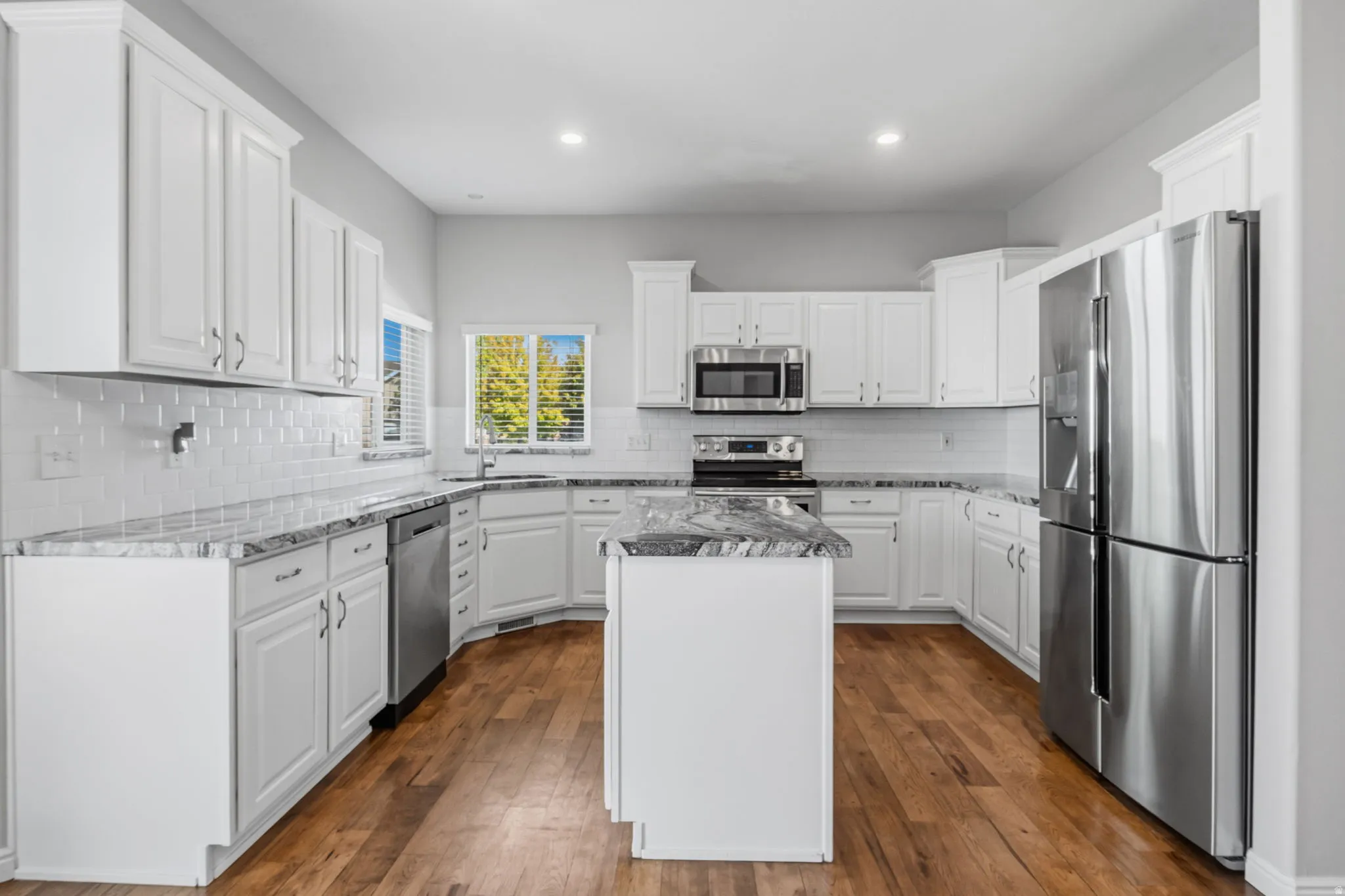 White cabinetry, stainless steel appliances, granite countertops, hardwood flooring, and a subway tile backsplash