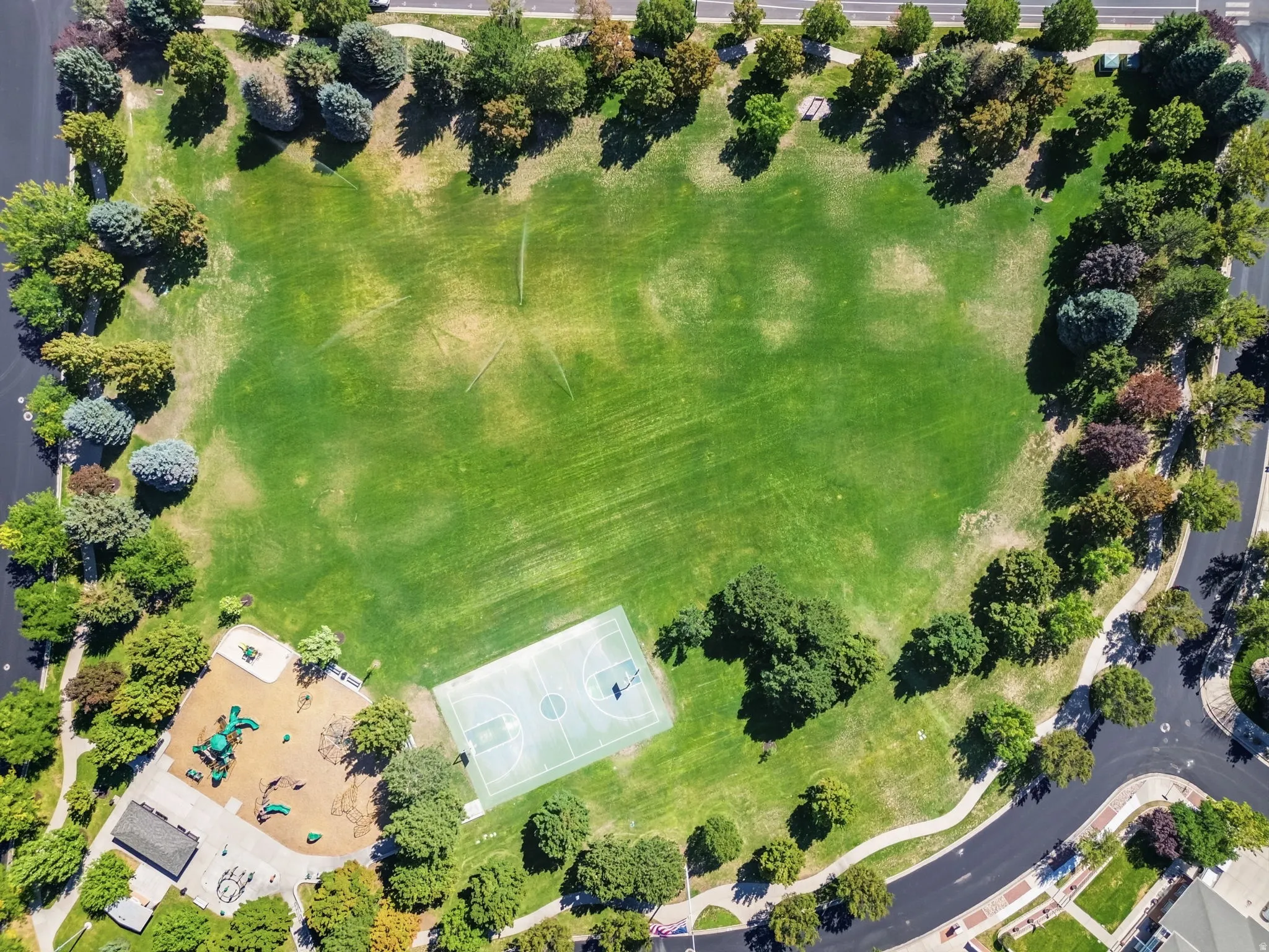 Expansive green space featuring a paved perimeter path, a basketball court, and a dedicated play area with equipment