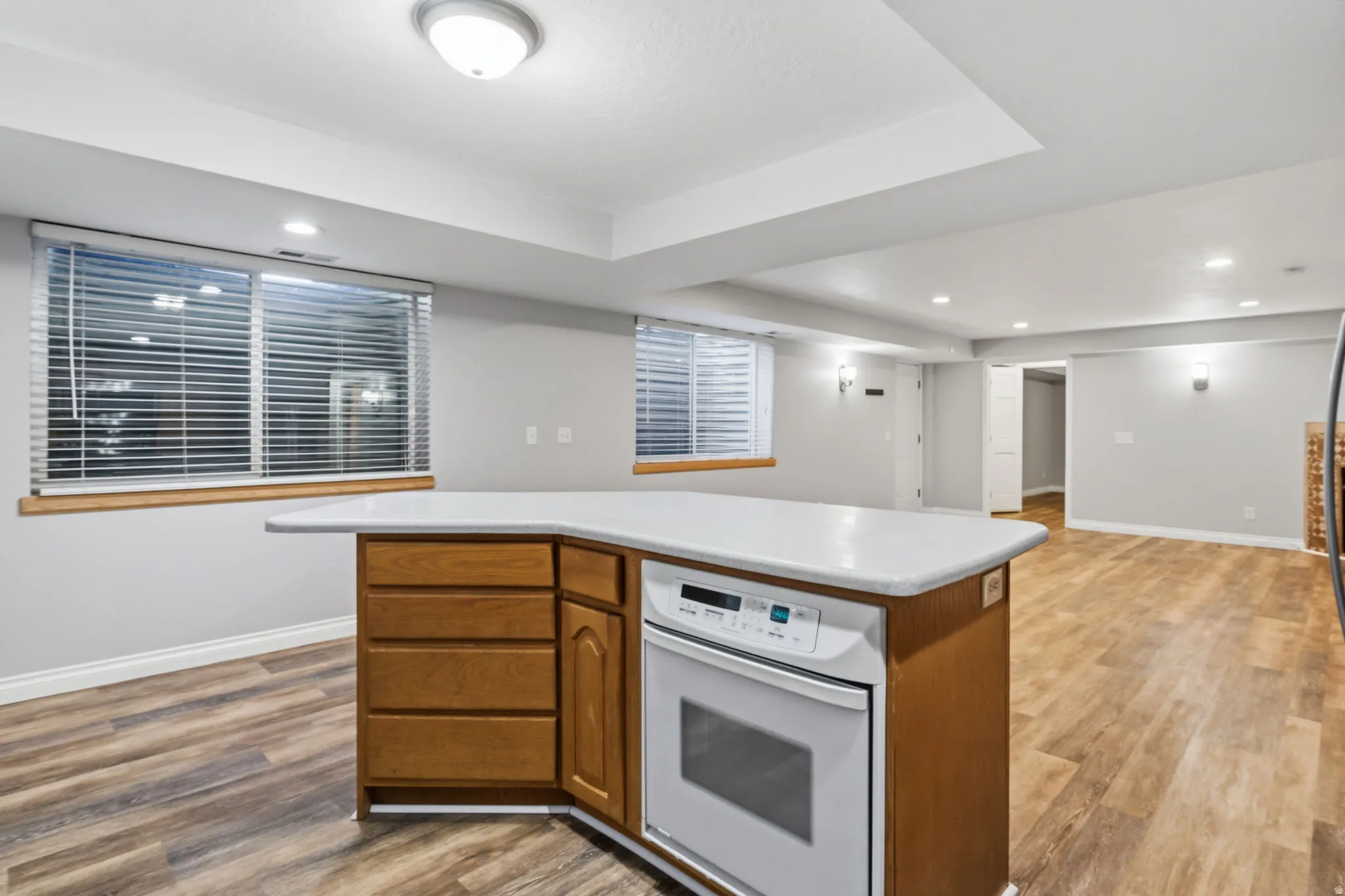 Kitchen island with wood-finish cabinetry, white countertop, and integrated oven