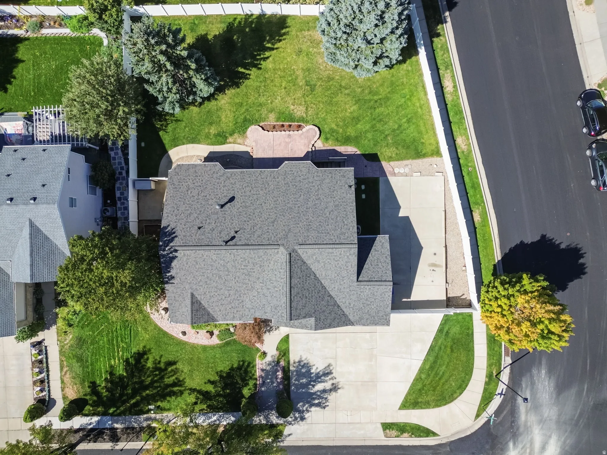 Expansive concrete driveway, mature landscaping, and well-maintained asphalt shingle roofing