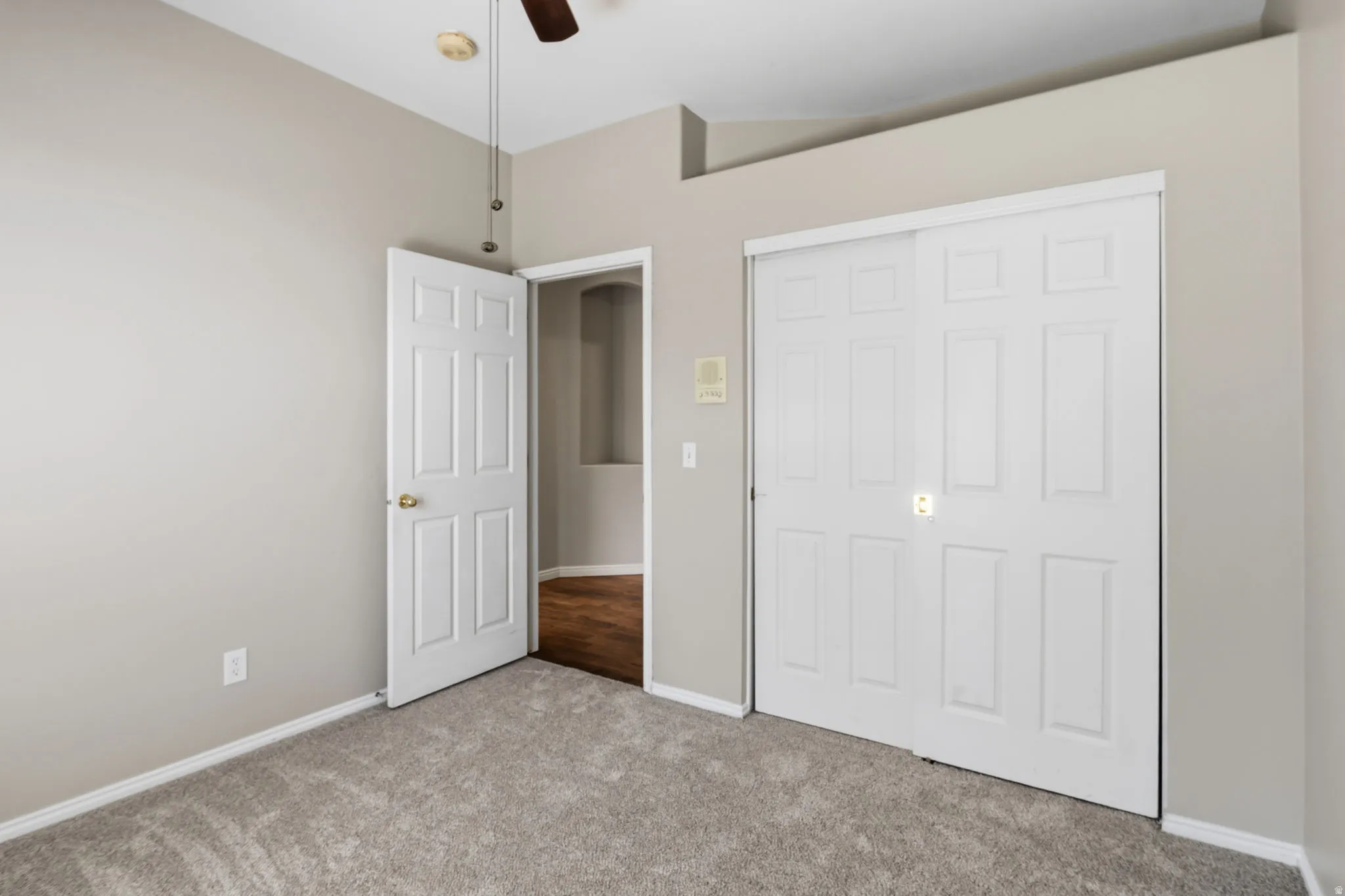 Neutral tone wall paint, carpeted flooring, paneled interior doors, and a ceiling fan with light fixture