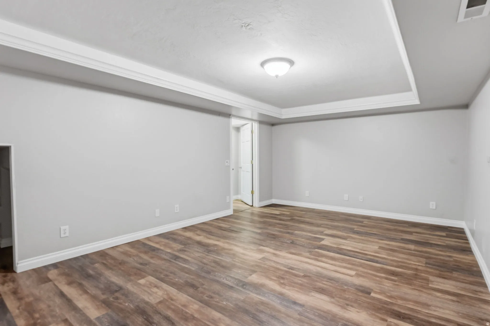 Expansive room featuring wood-finish flooring, light gray walls, white trim, and a tray ceiling with crown molding