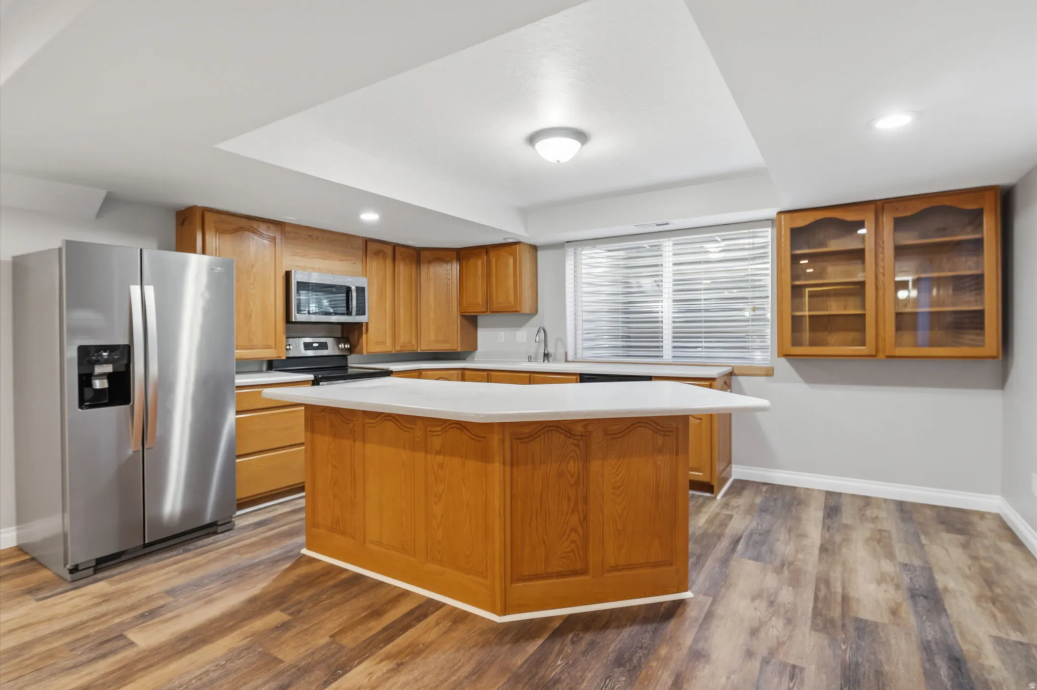 Kitchen featuring wood-finish flooring, recessed lighting, wood cabinetry, a center island with a light-toned countertop, and stainless steel appliances