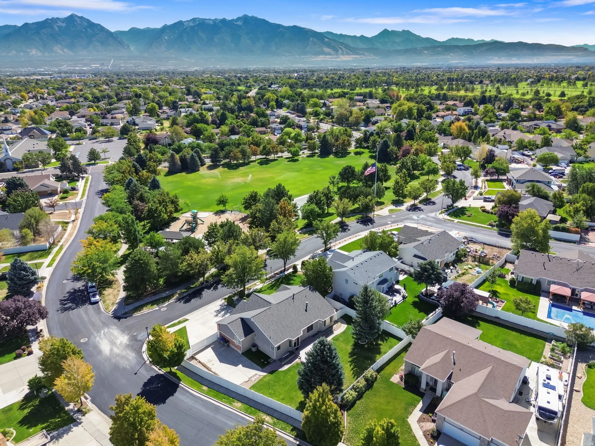 Expansive neighborhood green space, mature landscaping, tree-lined streets, mountain backdrop, and established residences