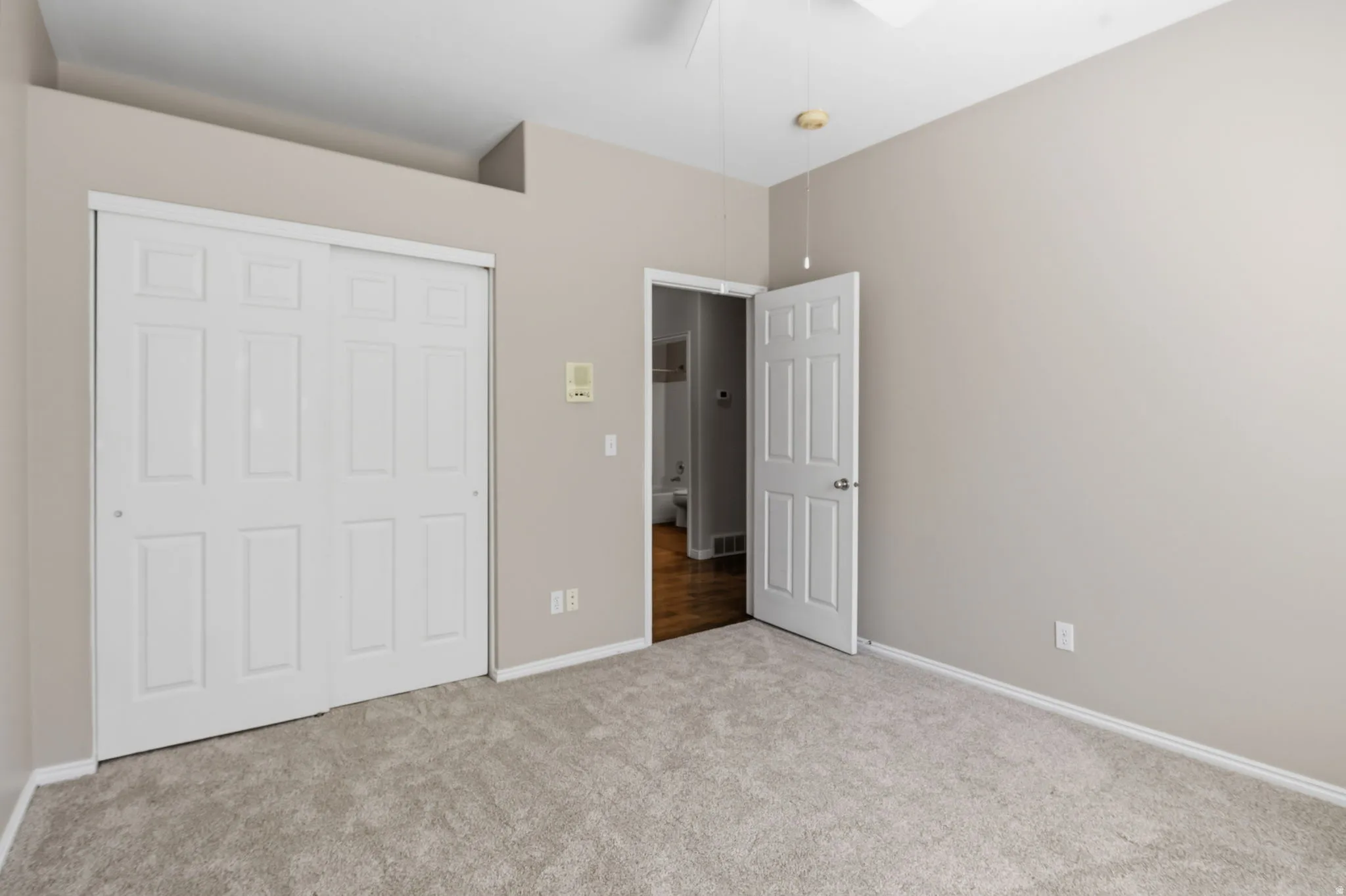 Neutral-toned walls, plush carpet flooring, white paneled closet doors, and a ceiling fan with integrated lighting