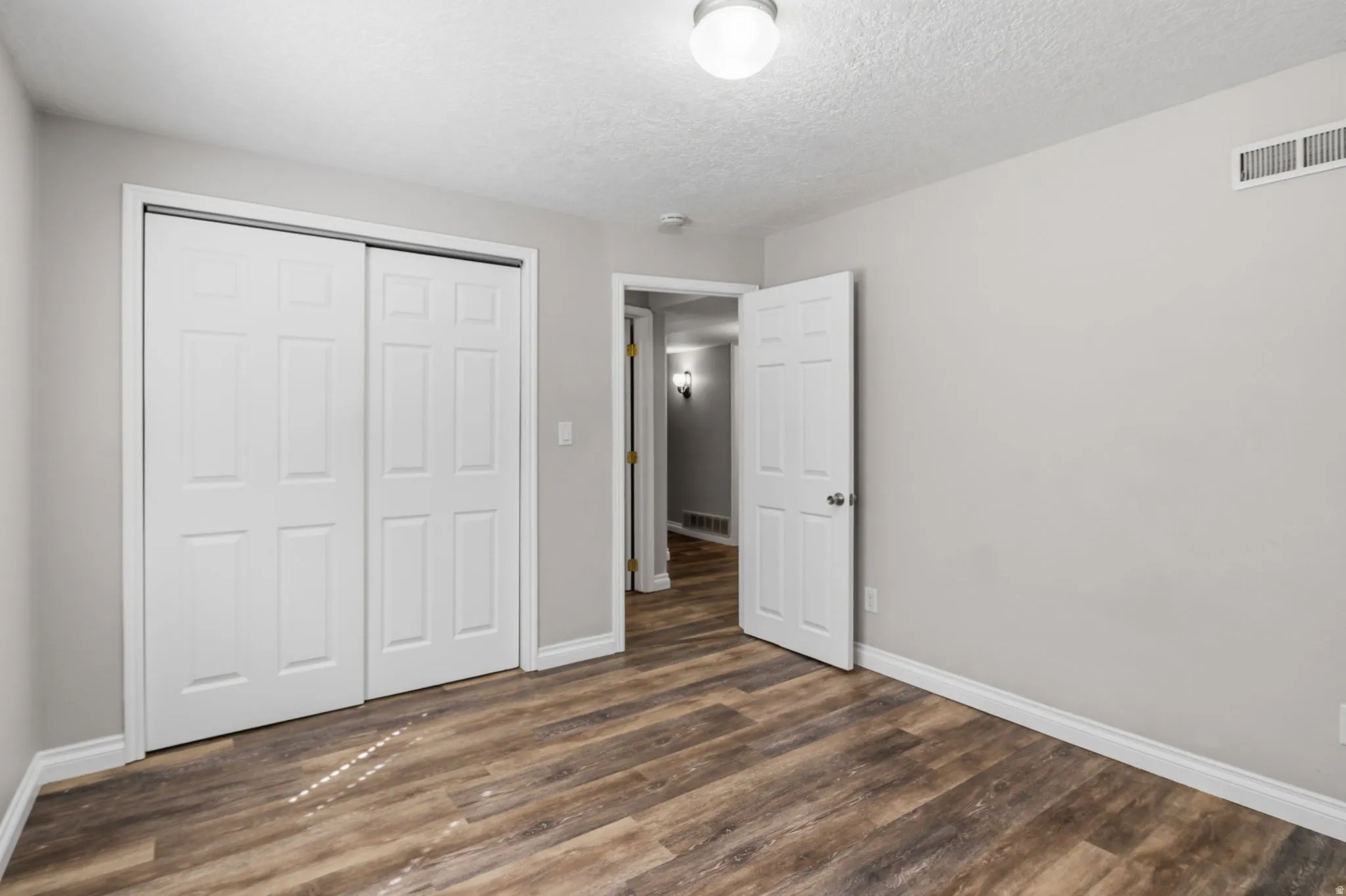Wood-finish flooring, white paneled doors, ceiling-mounted lighting, light gray wall finish, and white trim