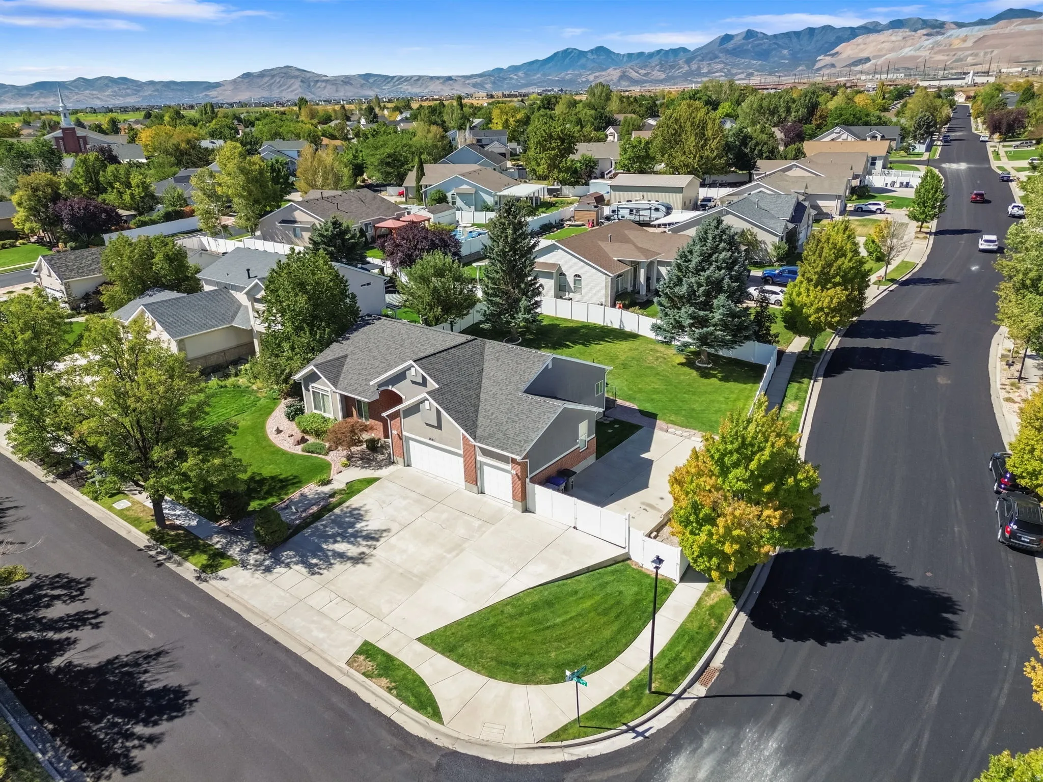 Corner lot property featuring a brick and siding exterior, a multi-car driveway, mature landscaping, and a mountain backdrop
