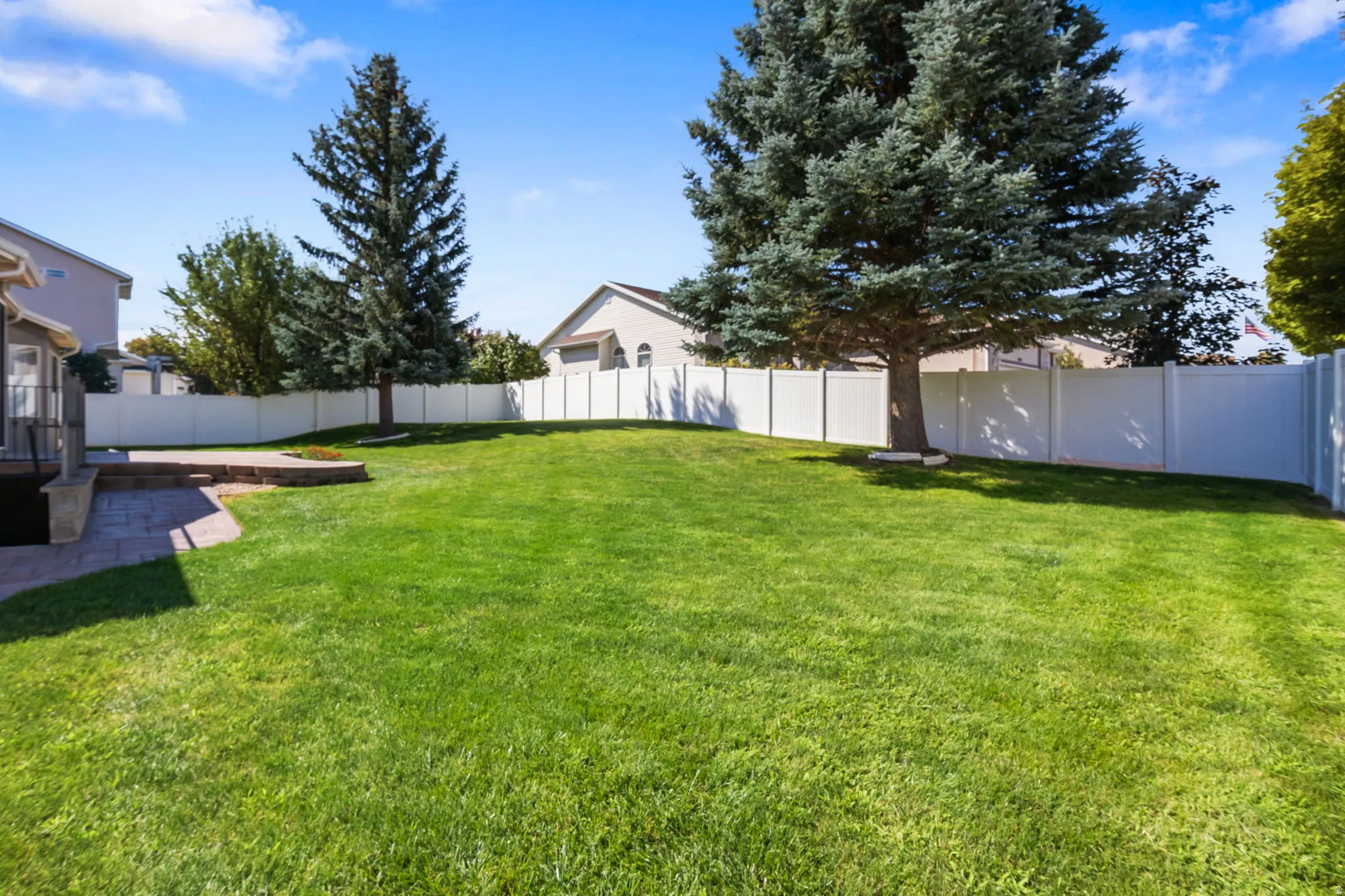 Expansive backyard featuring a lush lawn, mature trees, privacy fencing, and a paver patio with retaining wall