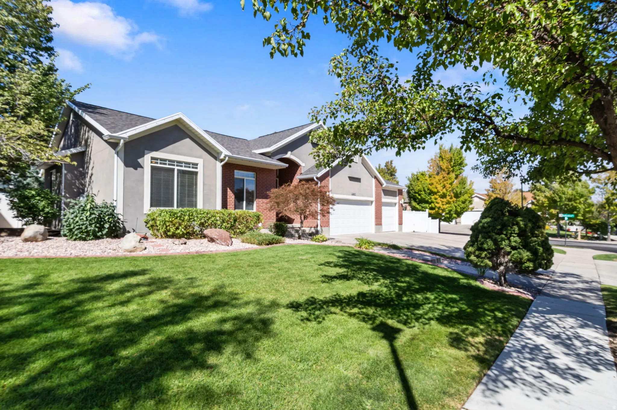 Residence with a stucco and brick facade, multiple garage doors, a concrete driveway, and a broad green lawn