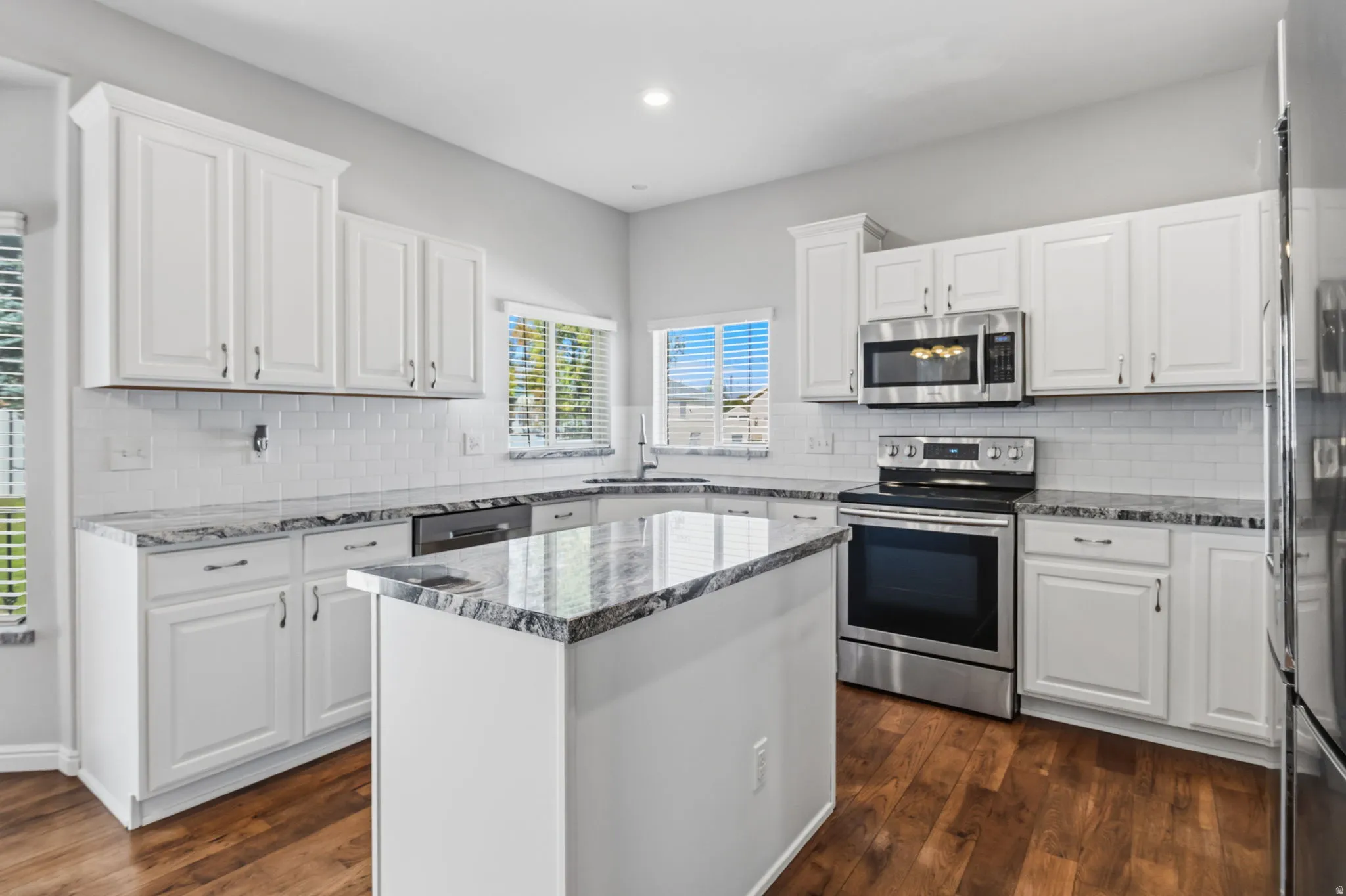 Kitchen featuring white shaker-style cabinetry, stainless steel appliances, granite countertops, and wood-finish flooring
