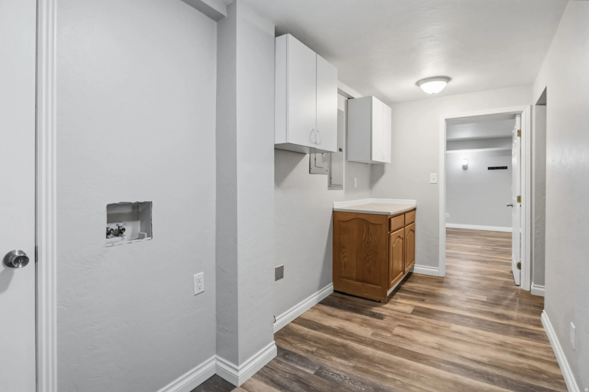 Laundry area featuring a wood-finish base cabinet with a solid surface countertop, white upper cabinetry, and wood-finish flooring