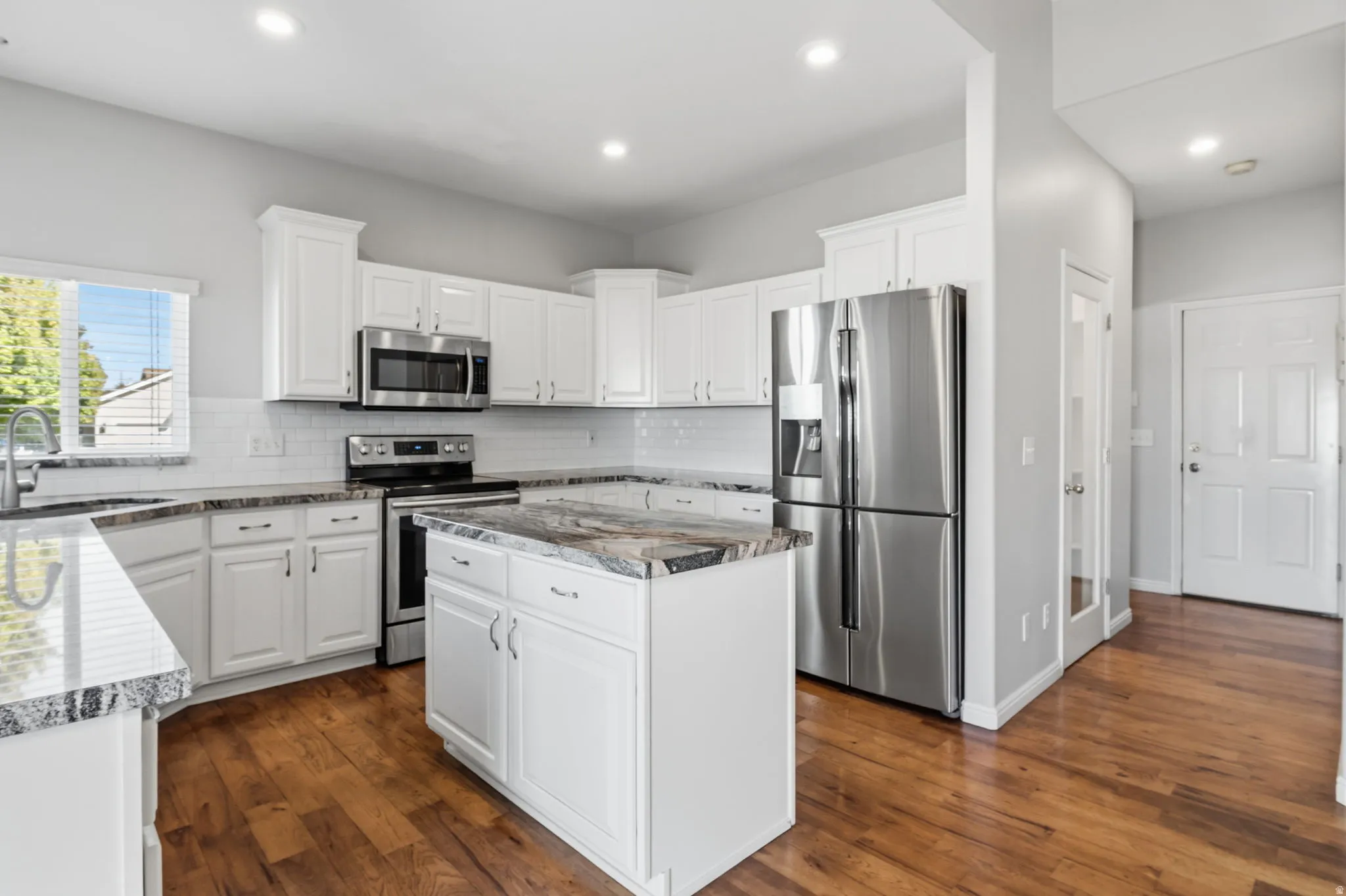 Kitchen featuring wood-finish flooring, white cabinetry, stainless steel appliances, and stone countertops