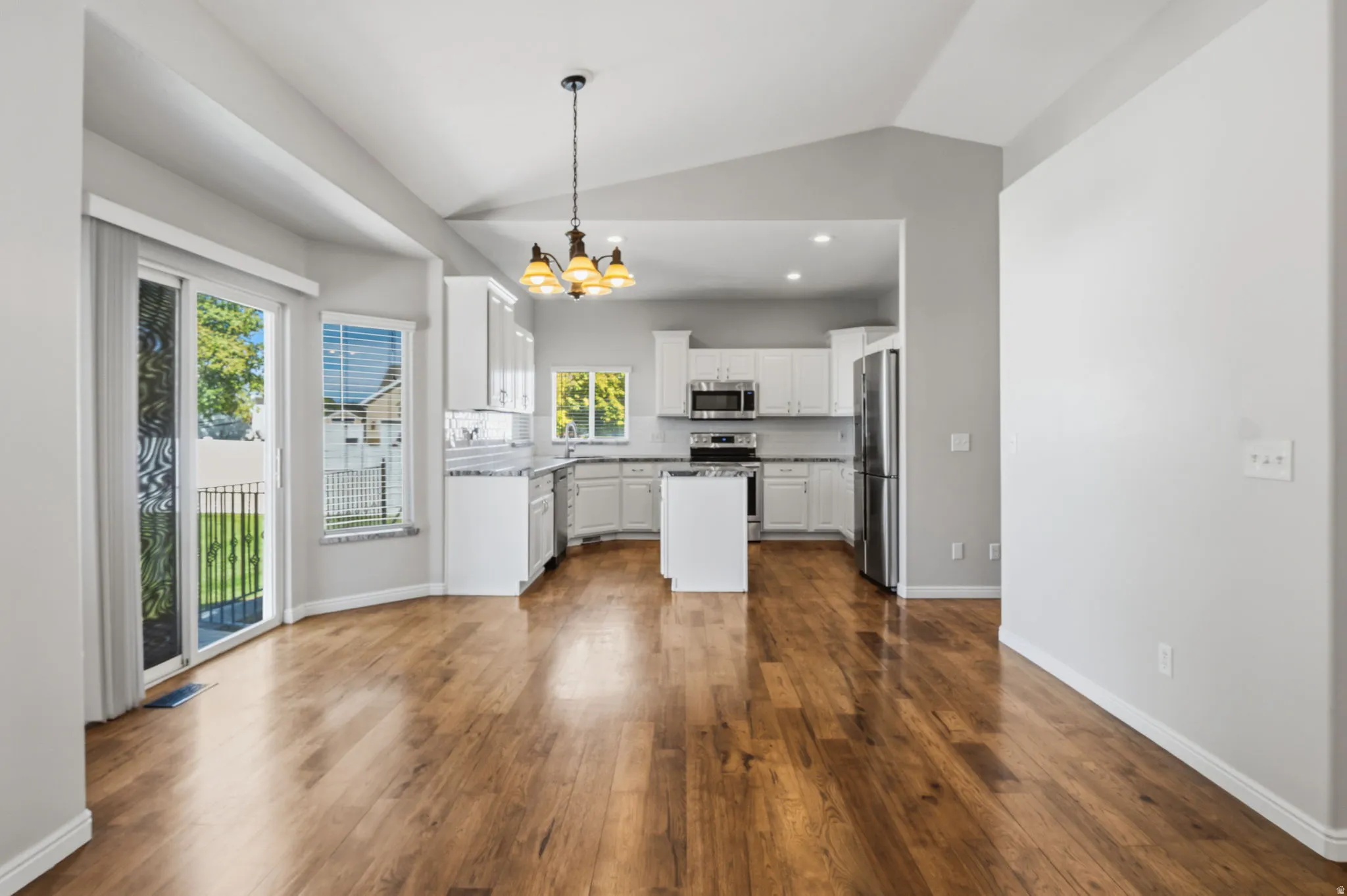Vaulted ceilings, wood-finish flooring, white cabinetry, stainless steel appliances, and a central kitchen island