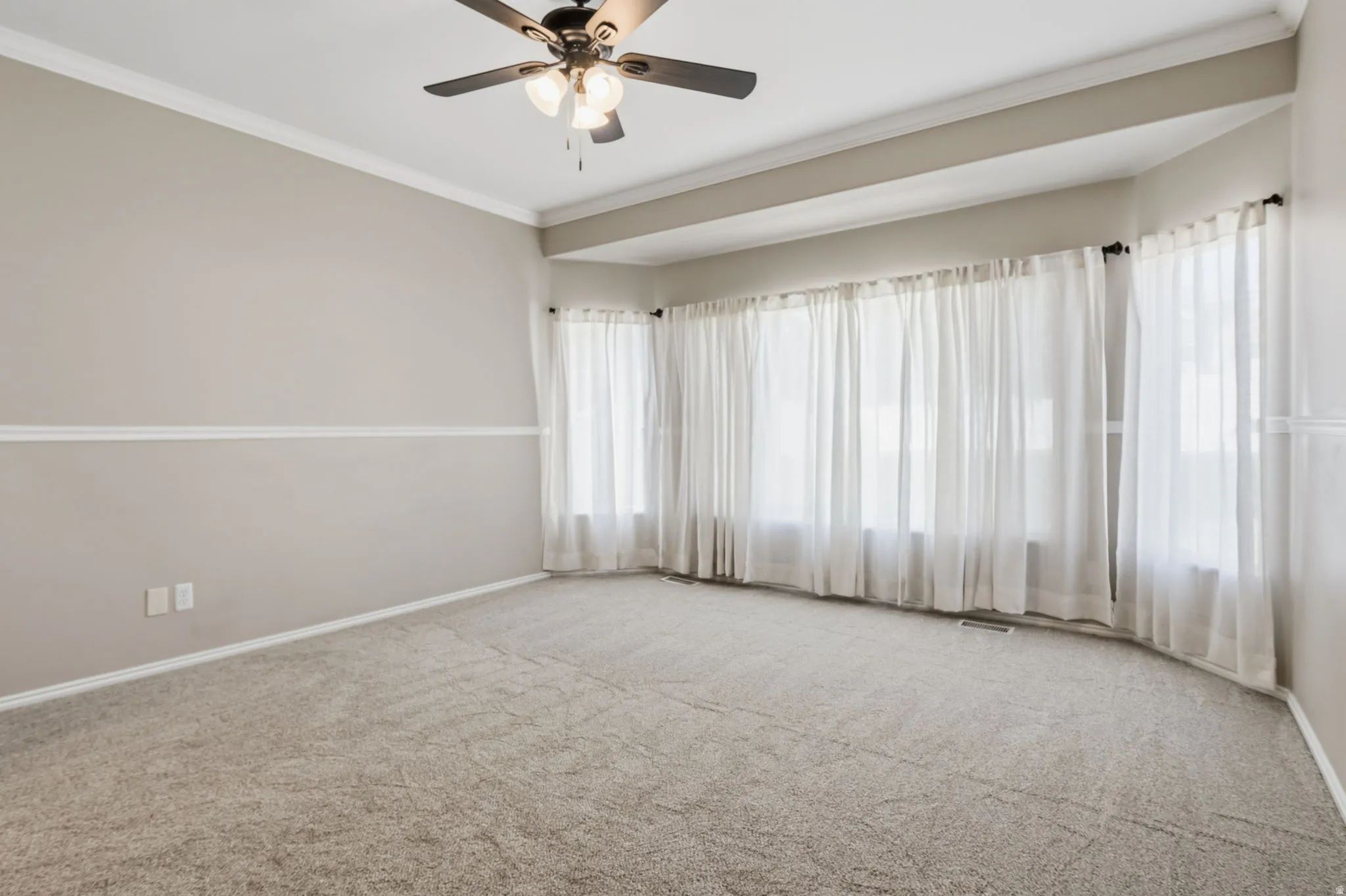 Recessed ceiling, neutral carpeting, ceiling fan, crown molding, and bay window