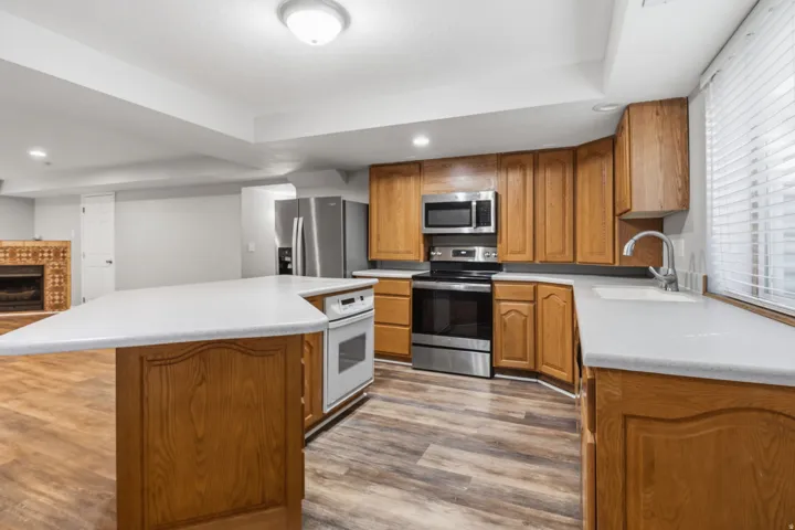 Kitchen featuring wood-finish flooring, stainless steel appliances, wood cabinetry, light-toned countertops, and an integrated oven