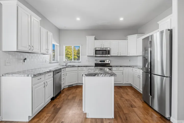 White cabinetry, stainless steel appliances, granite countertops, hardwood flooring, and a subway tile backsplash