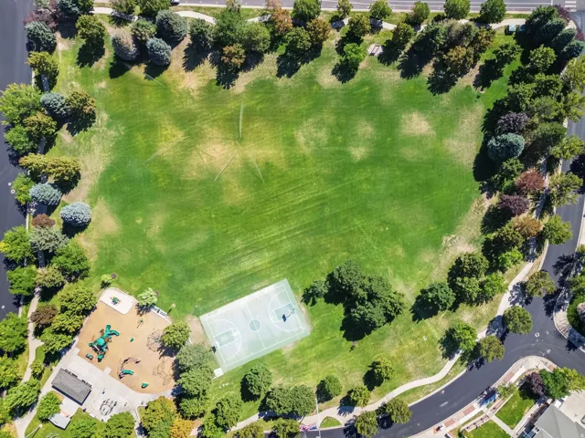 Expansive green space featuring a paved perimeter path, a basketball court, and a dedicated play area with equipment