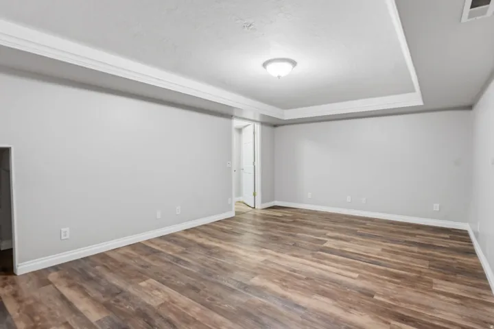 Expansive room featuring wood-finish flooring, light gray walls, white trim, and a tray ceiling with crown molding