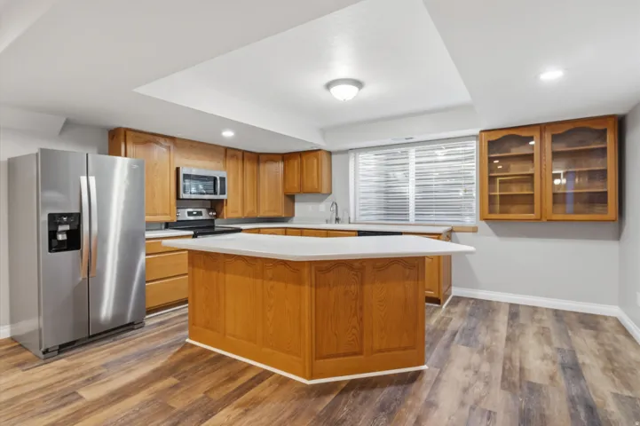 Kitchen featuring wood-finish flooring, recessed lighting, wood cabinetry, a center island with a light-toned countertop, and stainless steel appliances