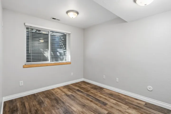 Wood-finish flooring, light gray walls, white trim, and a window with blinds