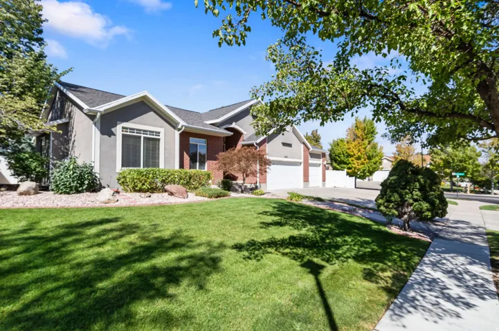 Residence with a stucco and brick facade, multiple garage doors, a concrete driveway, and a broad green lawn
