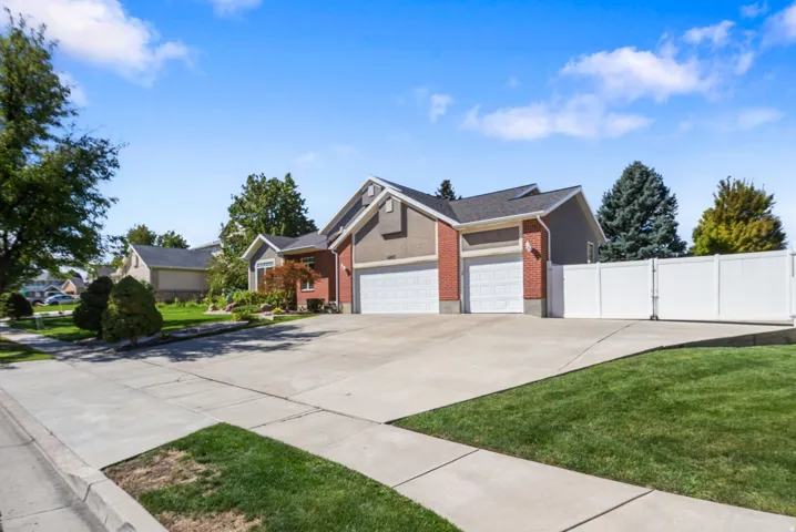 Brick and siding exterior with a multi-car driveway, two garage doors, and a white privacy fence