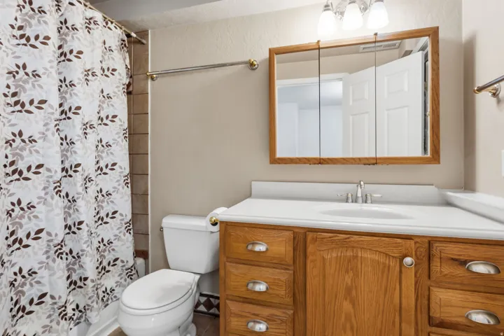 Wood-finish vanity with an integrated sink, polished chrome faucet, tri-fold mirrored medicine cabinet, and overhead vanity lighting
