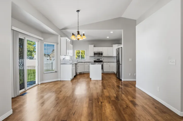 Vaulted ceilings, wood-finish flooring, white cabinetry, stainless steel appliances, and a central kitchen island