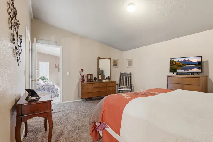 Spacious primary bedroom featuring hardwood dressers, carpeted flooring, recessed ceiling lighting, and a wall-mounted flat-screen television