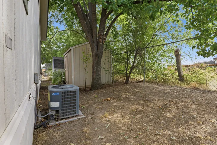 Spacious backyard with mature shade trees and natural landscaping, complemented by a detached storage structure and HVAC unit positioned on the grounds