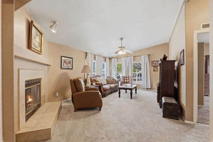 Living area featuring a vaulted ceiling with a ceiling fan, a tiled fireplace, and multiple windows