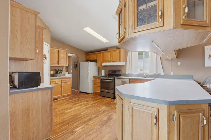 Spacious kitchen featuring wood cabinetry, stainless steel appliances, wood-finish flooring, and ample counter space with a curved island