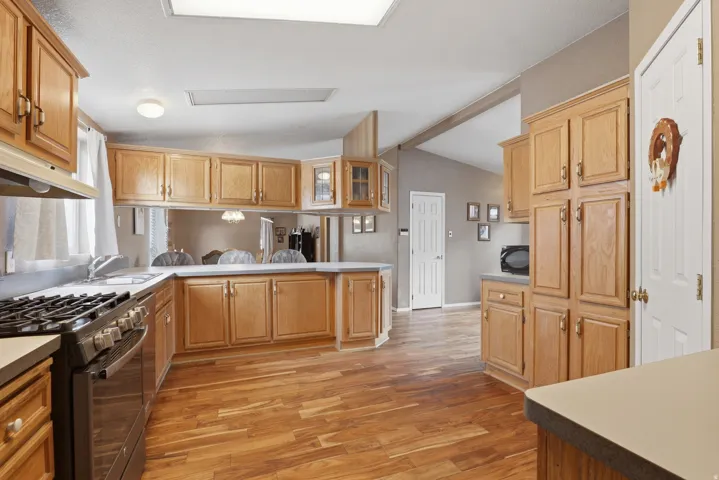 Spacious kitchen featuring honey-toned wood cabinetry, stainless steel appliances including a gas range, wood-finish flooring throughout, recessed ceiling lighting, and a large center island with quartz countertop