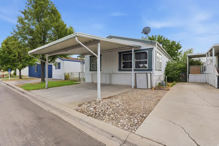 Charming mobile home featuring a covered front porch with metal roof overhang, large picture windows, and a gravel landscaped yard