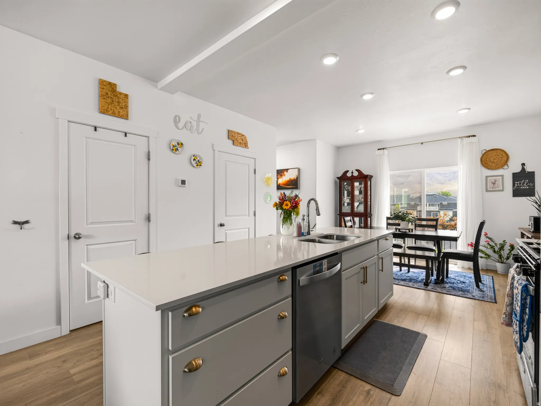Kitchen island with integrated sink, stainless steel dishwasher, light wood-finish flooring, recessed ceiling lighting, and a dining area