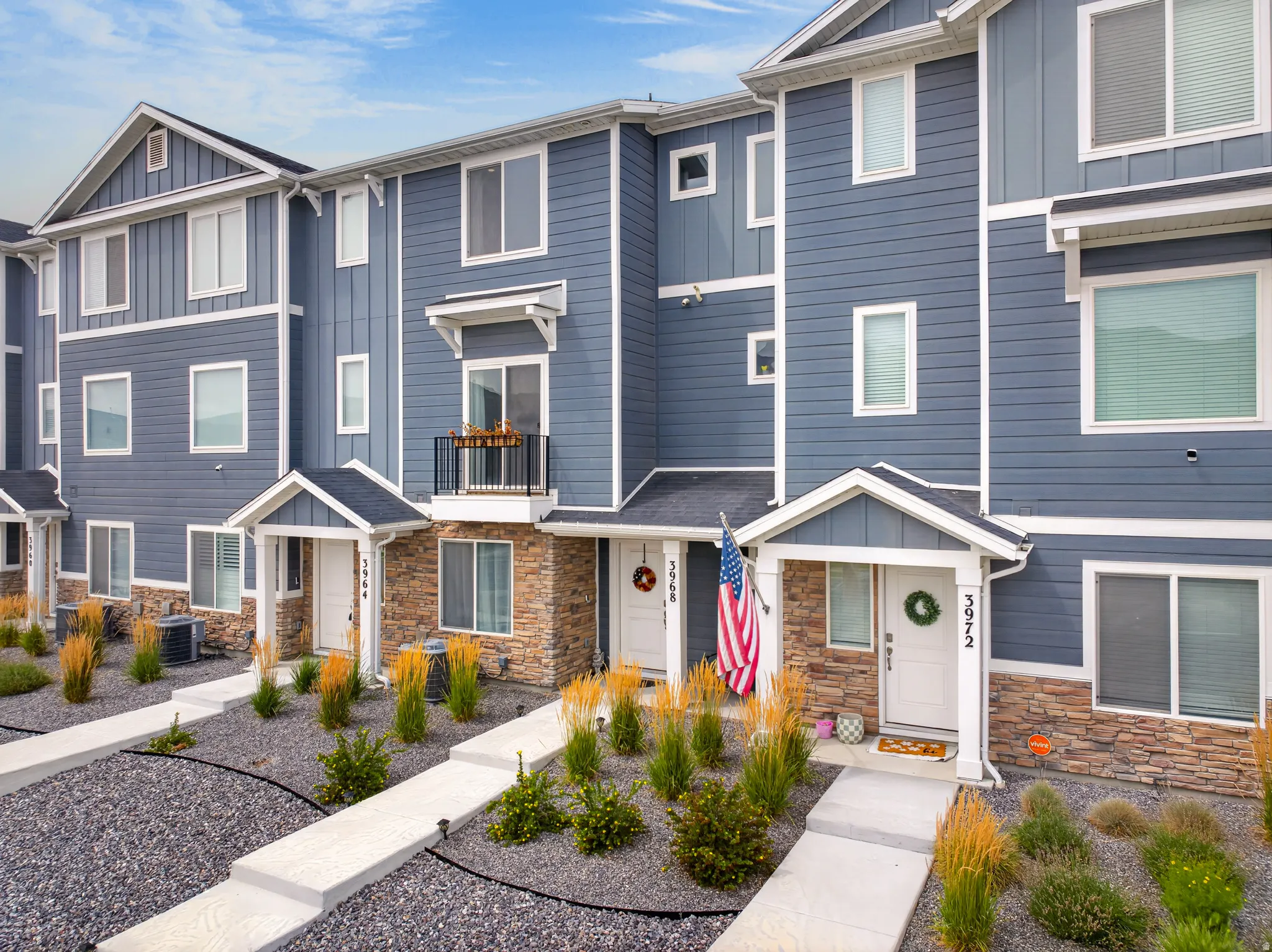 Modern townhome exterior featuring blue siding, white trim, stone accents, and multiple windows
