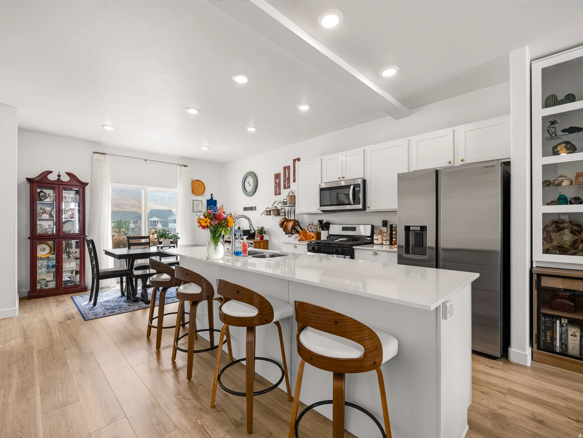 Open-concept kitchen featuring white cabinetry, stainless steel appliances, a center island with countertop seating, recessed lighting, and wood-finish flooring