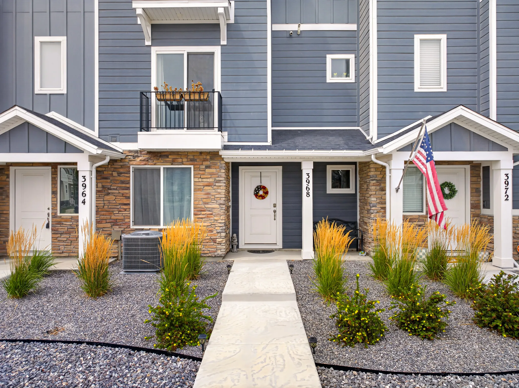 Exterior featuring gray siding, stone veneer accents, individual front entrances, and a second-story balcony with metal railing