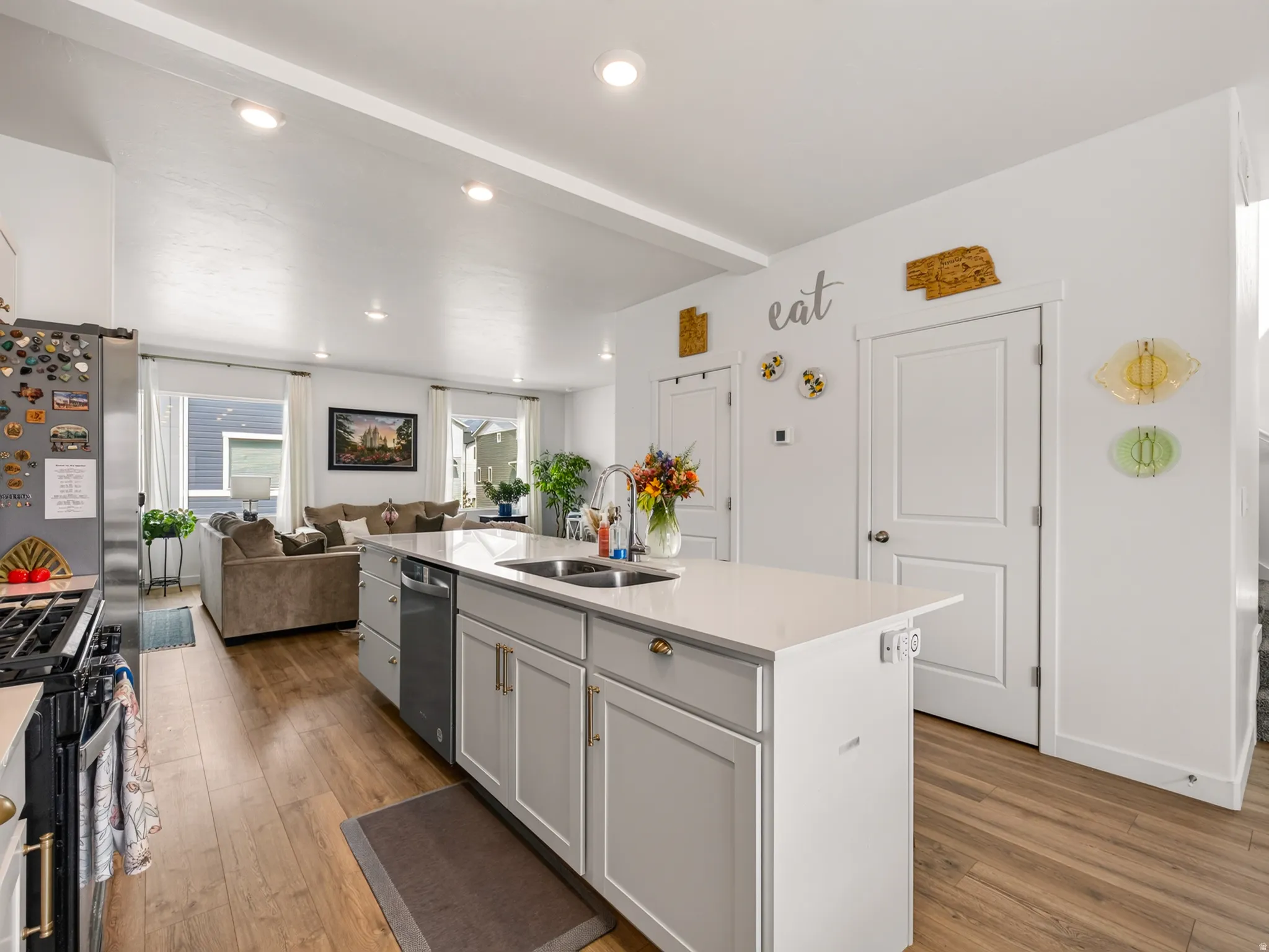 Open-concept kitchen and living area featuring a large center island with a sink, stainless steel appliances, recessed lighting, and wood-finish flooring