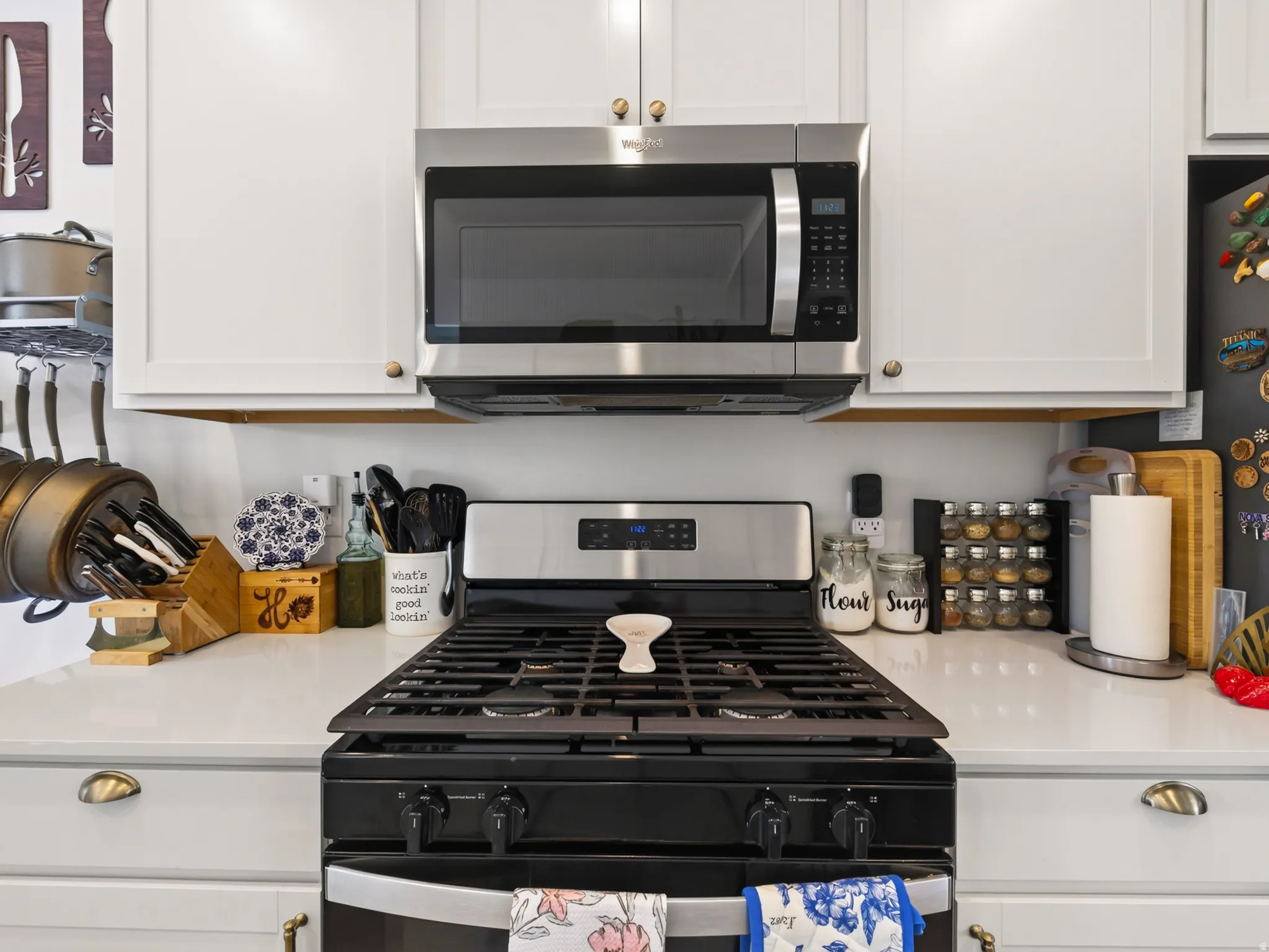 White cabinetry with gold-tone hardware, stainless steel microwave, stainless steel range with black cooktop, white countertop