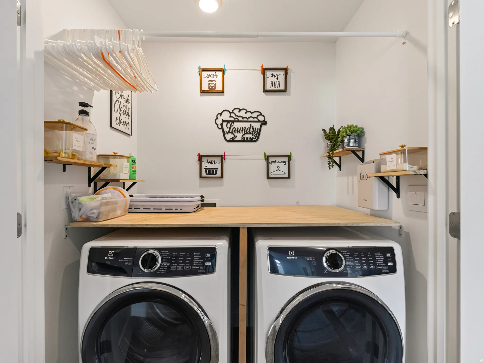 Built-in laundry closet with a wood-finish countertop, dual front-load appliances, wall-mounted shelving, and an overhead clothes rod
